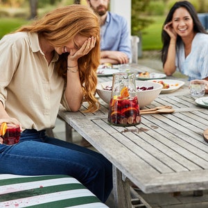 May include: A group of friends enjoying a meal outdoors. A woman is laughing while holding a glass of red wine. A pitcher of sangria with fruit and ice is on the table.