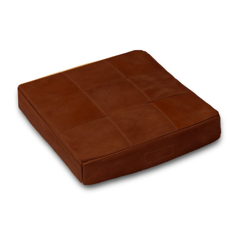 May include: A brown leather square cushion with a quilted design. The cushion is filled with a soft material and has a smooth, comfortable surface.