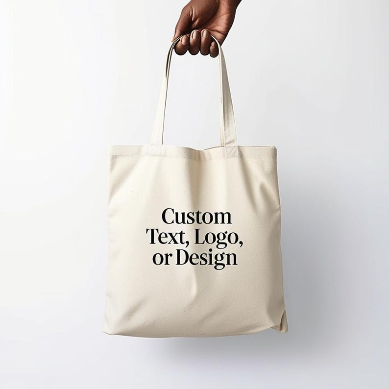 Puede incluir: Una bolsa de lona blanca con texto negro que dice "Custom Text, Logo, or Design".