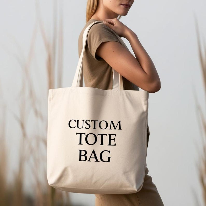 Puede incluir: Una bolsa de lona blanca con texto negro que dice "CUSTOM TOTE BAG".