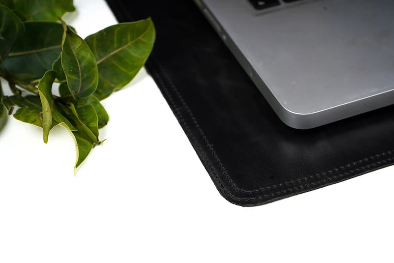 Black leather desk mat under a laptop with a plant