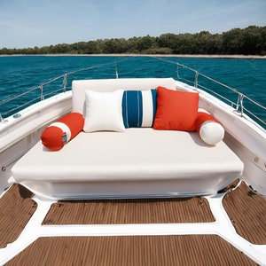 Peut inclure: Un si&egrave;ge de bateau blanc avec des coussins ray&eacute;s rouge, blanc et bleu. Le bateau est amarr&eacute; dans un plan d'eau calme avec des arbres verts en arri&egrave;re-plan.