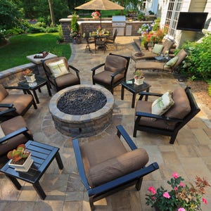 May include: An outdoor patio setting with a fire pit at the center, surrounded by dark brown armchairs with brown cushions. Small black side tables and a dining set are also present. The patio is paved with stone.