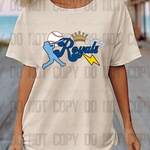 May include: A white t-shirt with a blue and white baseball graphic, a crown, a diamond, and the text "Royals" in blue.