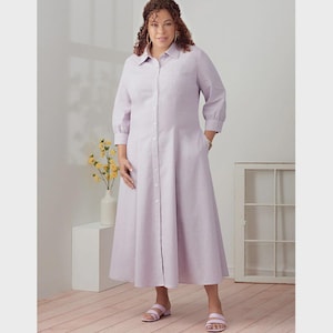Può includere: Un abito camicia lilla chiaro con colletto, maniche lunghe e gonna svasata. L'abito ha tasche e viene indossato con sandali rosa. Un vaso di fiori gialli è sullo sfondo.
