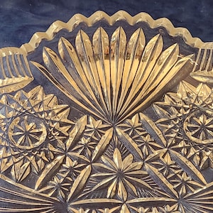 May include: Close-up of a clear glass bowl with intricate, geometric patterns. The bowl has a scalloped rim and a central design resembling a stylized sunburst. The detailed carvings create a play of light and shadow, enhancing the bowl's decorative appeal.