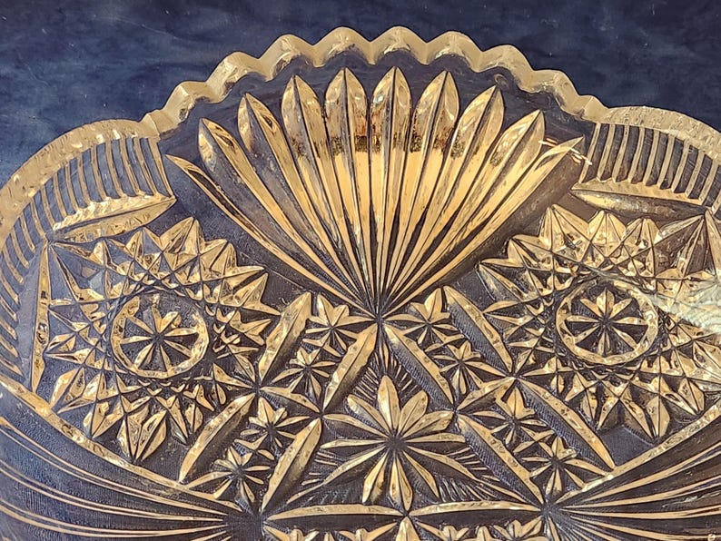 May include: Close-up of a clear glass bowl with intricate, geometric patterns. The bowl has a scalloped rim and a central design resembling a stylized sunburst. The detailed carvings create a play of light and shadow, enhancing the bowl's decorative appeal.