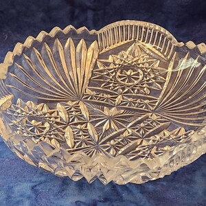 May include: A clear, cut-glass bowl with a scalloped edge. The bowl has intricate geometric and fan-shaped patterns. The design is symmetrical, with a starburst pattern in the centre. A decorative piece for serving or display.