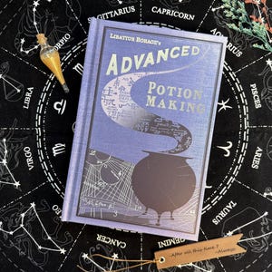 Peut inclure: Un livre relié intitulé Libatius Borage's Advanced Potion Making avec une couverture bleue ornée d'un chaudron noir, de fumée tourbillonnante et de schémas techniques. Une petite fiole en verre avec un liquide doré et une étiquette brune.