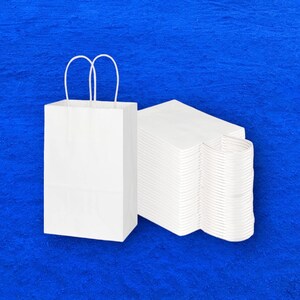 Op de afbeelding: Een witte papieren tas met handvatten en een stapel witte papieren tassen.