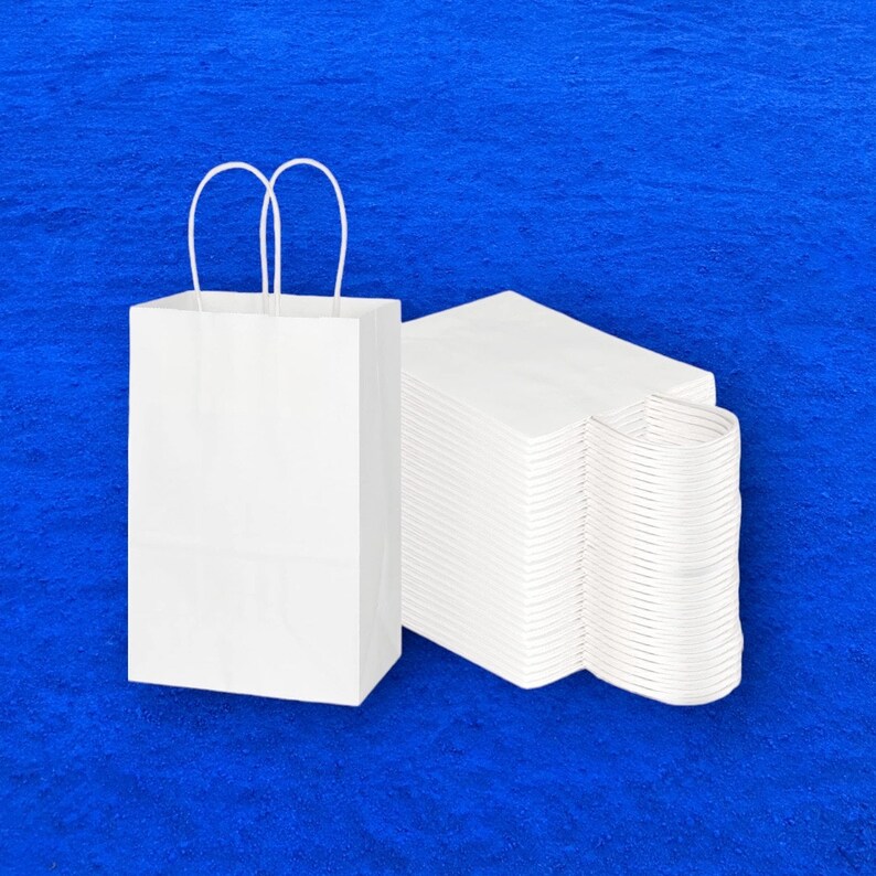 Op de afbeelding: Een witte papieren tas met handvatten en een stapel witte papieren tassen.