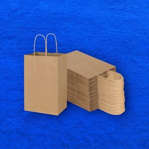 Op de afbeelding: Een stapel bruine papieren tassen met handvatten. De tassen zijn gevouwen en op elkaar gestapeld. De tassen staan op een blauwe achtergrond.