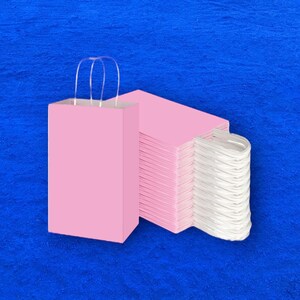 Op de afbeelding: Een stapel roze papieren cadeauzakken met witte handvatten. De zakken zijn gevouwen en op elkaar gestapeld. De zakken bevinden zich op een blauwe achtergrond.