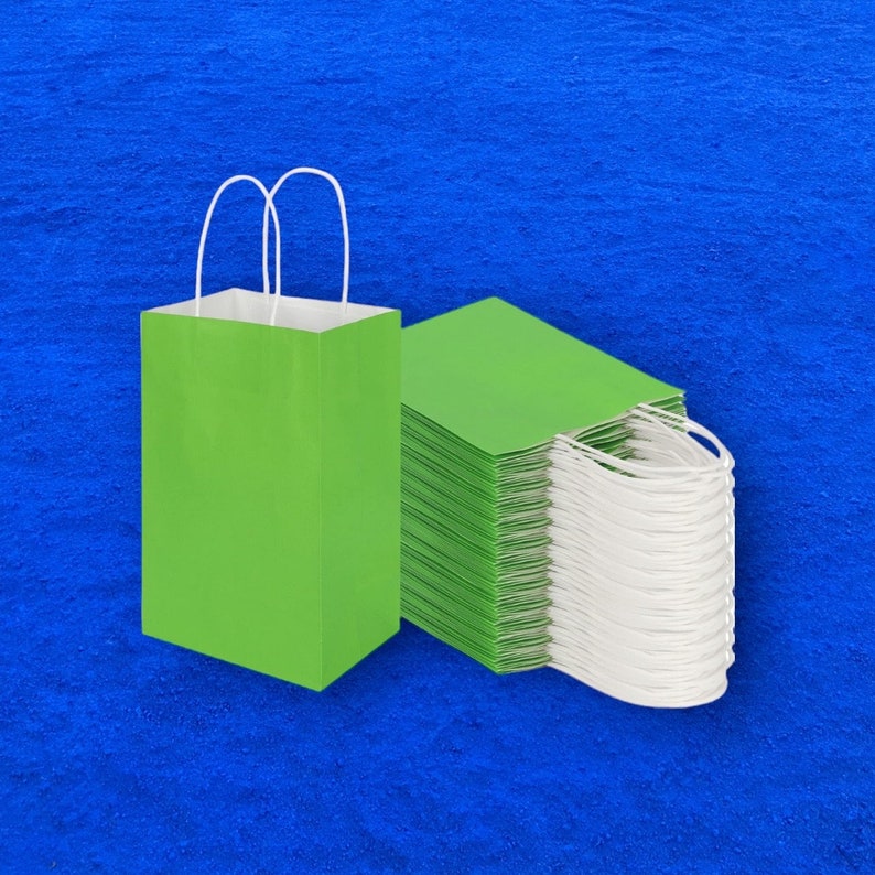 Op de afbeelding: Een stapel groene papieren cadeauzakken met witte handvatten. De zakken zijn plat gevouwen en klaar voor gebruik.