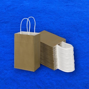 Op de afbeelding: Een stapel bruine papieren zakken met witte handvatten. De zakken zijn netjes gestapeld, met de handvatten naar buiten. De zakken liggen op een blauw oppervlak.