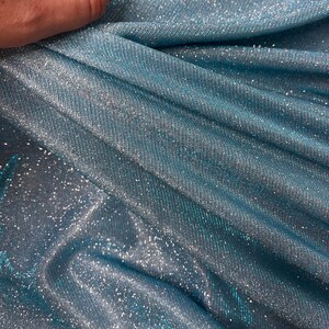 May include: Close-up of a blue fabric with silver glitter woven into the material. The fabric is folded and draped, showing the texture and shimmer.