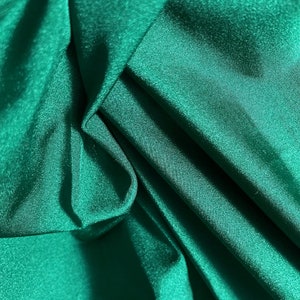 May include: A close-up of a smooth, emerald green fabric with a subtle sheen. The fabric is folded and draped, showcasing its texture and colour.