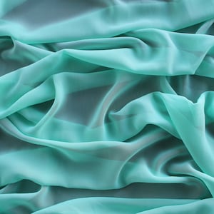 May include: A close-up of a light turquoise fabric with soft, flowing folds. The fabric is smooth and silky, with a delicate sheen.