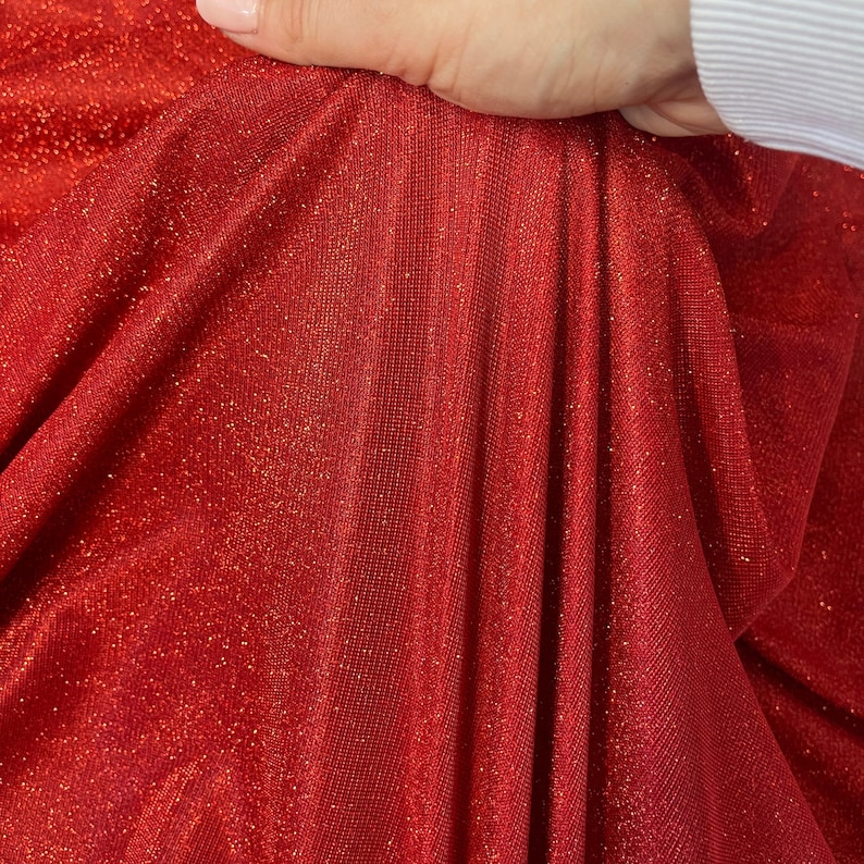 May include: Red sparkly fabric with a fine, shimmery texture. The fabric is soft and drapes nicely.