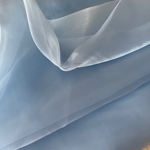 May include: A light blue sheer fabric with a soft, flowing texture. The fabric is folded in half, creating a smooth, even surface.