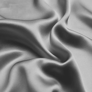 May include: A smooth, silky fabric in a light gray color. The fabric is draped and folded, creating soft, flowing curves.