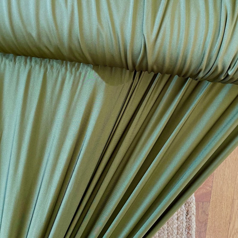 May include: Close-up of a green fabric with a smooth, silky texture. The fabric is folded and draped, creating soft folds and curves.