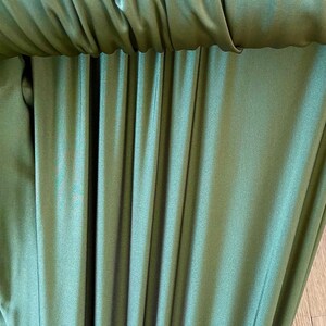 May include: Close-up of a green fabric with a smooth, silky texture. The fabric is folded and draped, creating a series of vertical lines.