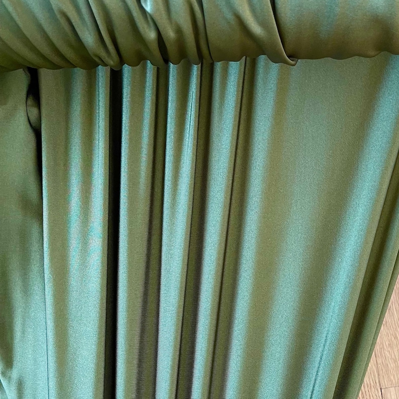 May include: Close-up of a green fabric with a smooth, silky texture. The fabric is folded and draped, creating a series of vertical lines.