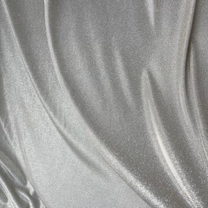May include: Silver fabric with a subtle shimmer and a textured, ribbed pattern. The fabric is draped and folded, creating soft curves and folds.