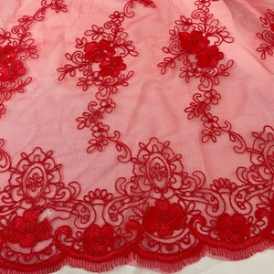 May include: Red embroidered lace fabric with a floral design. The lace has a scalloped edge.