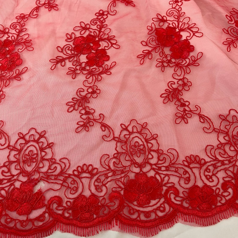 May include: Red embroidered lace fabric with a floral design. The lace has a scalloped edge.