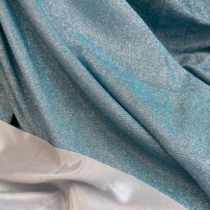 May include: A close-up of a teal fabric with a silver shimmer. The fabric is folded and has a white fabric underneath.