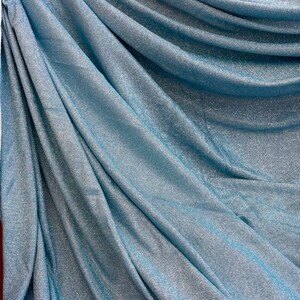 May include: A close-up of a light blue fabric with a sparkly, shimmery texture. The fabric is folded and draped, showcasing its soft and flowing nature.