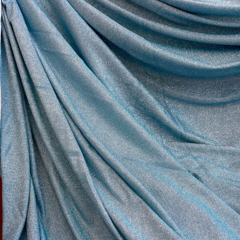 May include: A close-up of a light blue fabric with a sparkly, shimmery texture. The fabric is folded and draped, showcasing its soft and flowing nature.