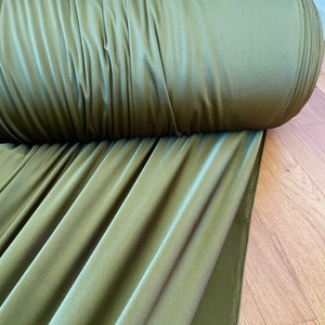 May include: A roll of olive green fabric with a smooth, silky texture. The fabric is folded and draped on a wooden surface.