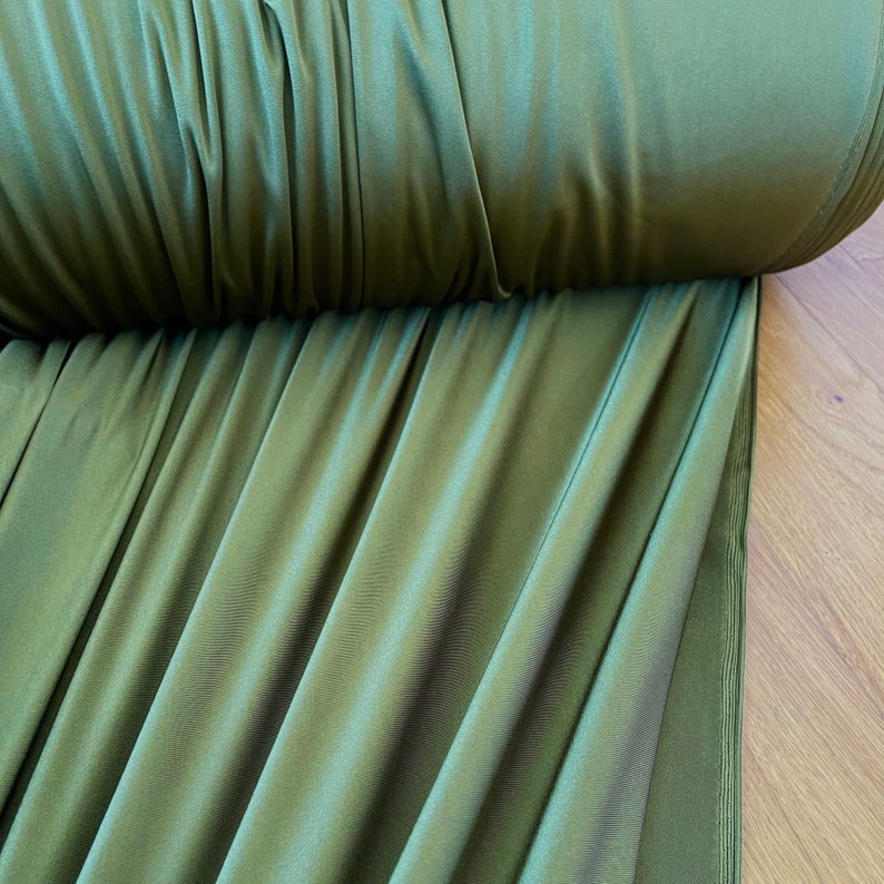 May include: Close-up of a roll of olive green fabric with a smooth, silky texture. The fabric is folded and draped, showcasing its drape and flow.
