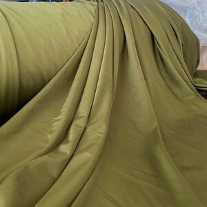 May include: A close-up of a smooth, olive green fabric. The fabric is draped and folded, showing its texture and color.