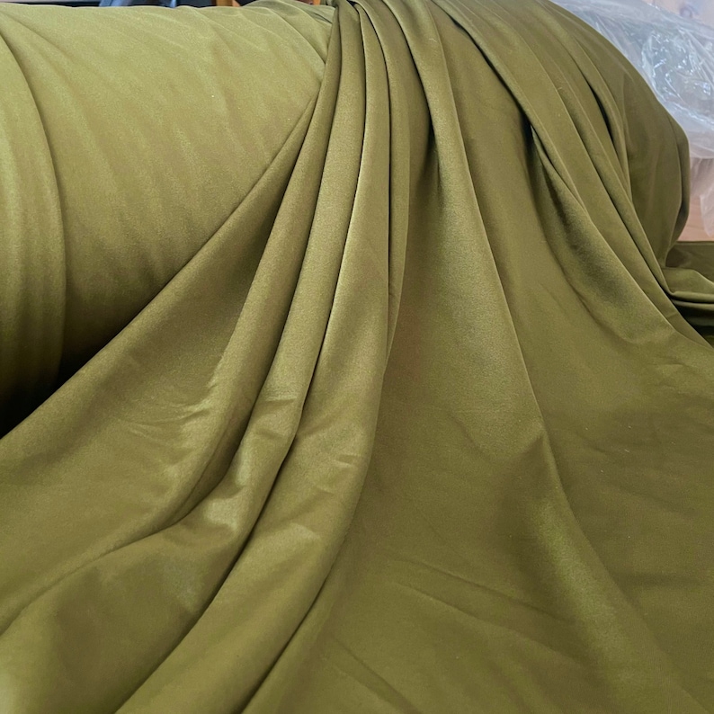 May include: A close-up of a smooth, olive green fabric. The fabric is draped and folded, showing its texture and color.