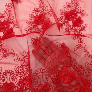 May include: Red sheer fabric with delicate floral embroidery. The fabric is soft and lightweight, making it perfect for a variety of projects.