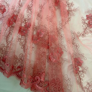 May include: Pink floral lace fabric with a delicate pattern. The lace is sheer and has a soft, romantic feel.