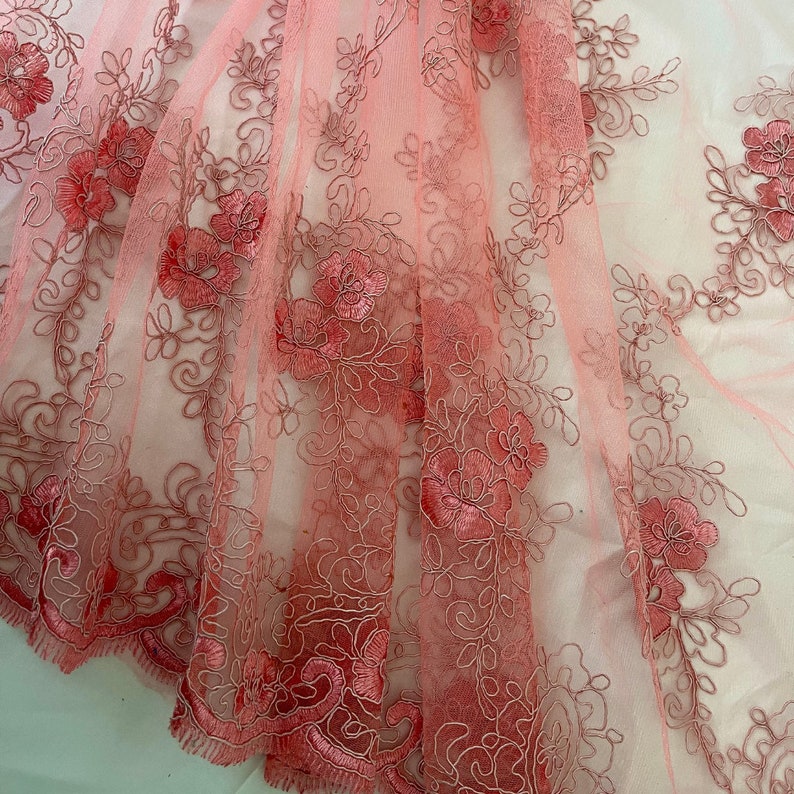 May include: Pink floral lace fabric with a delicate pattern. The lace is sheer and has a soft, romantic feel.