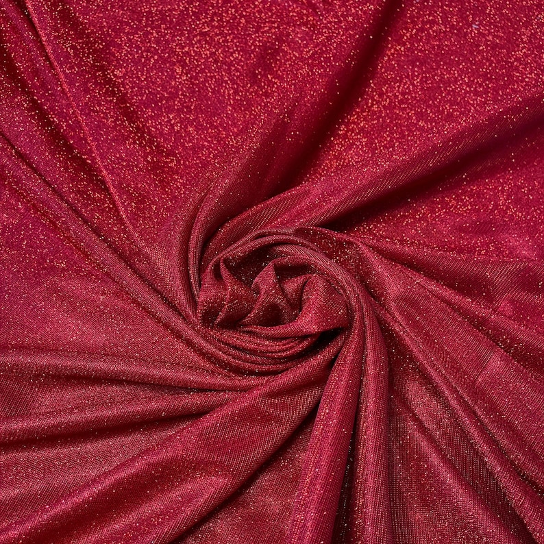 May include: Red sparkly fabric with a textured, woven pattern. The fabric is gathered and folded, creating a soft, flowing look.