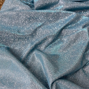 May include: Close-up of a light blue fabric with a sparkly, iridescent finish. The fabric has a subtle ribbed texture.