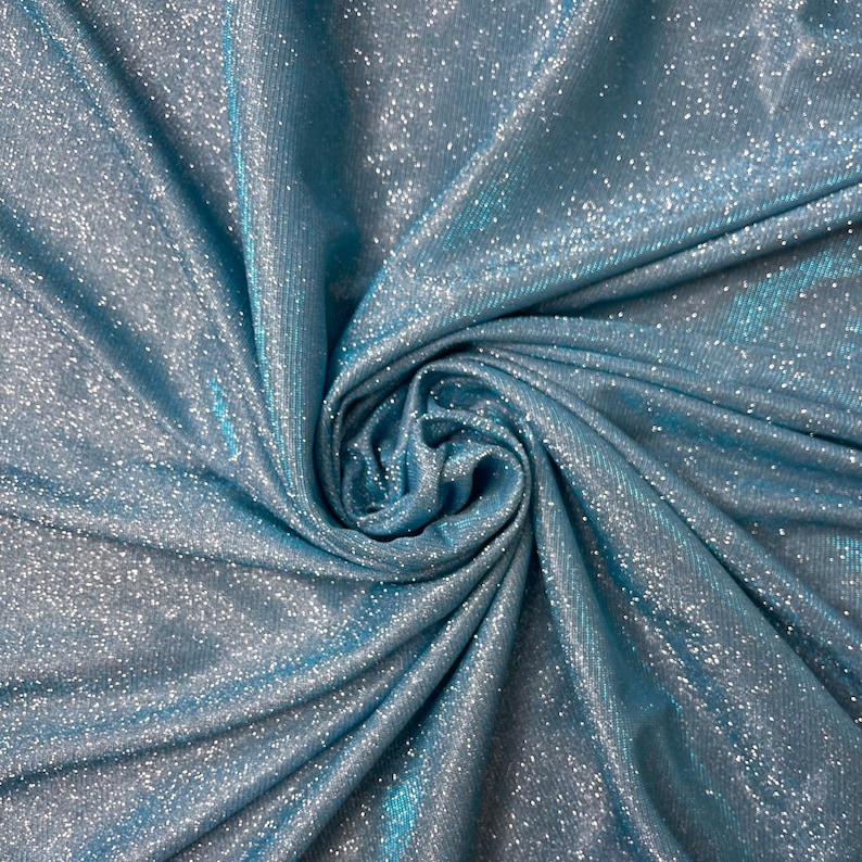 May include: A close-up of a light blue fabric with a sparkly, iridescent finish. The fabric is wrinkled and folded, creating a textured and abstract pattern.