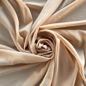 May include: A close-up of a beige sheer fabric, draped and folded to create a soft, swirling pattern.