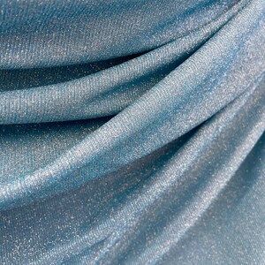 May include: Close-up of a blue fabric with a shimmery, glittery texture. The fabric is folded and draped, creating soft folds and curves.