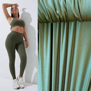 May include: A woman wearing a green sports bra and matching leggings. The leggings are made of a smooth, shiny fabric.