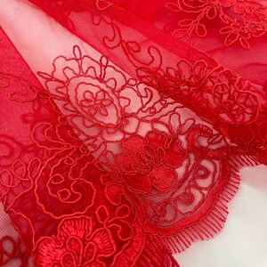 May include: Red lace fabric with a floral pattern. The lace is delicate and intricate, with a scalloped edge.