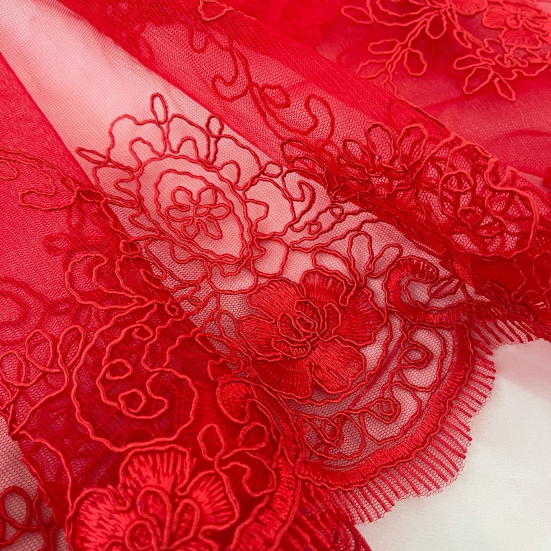May include: Red lace fabric with a floral pattern. The lace is delicate and intricate, with a scalloped edge.