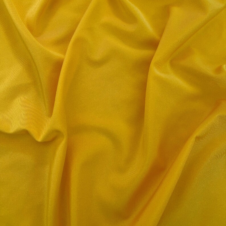 May include: A close-up of a smooth, yellow fabric with soft folds and wrinkles.